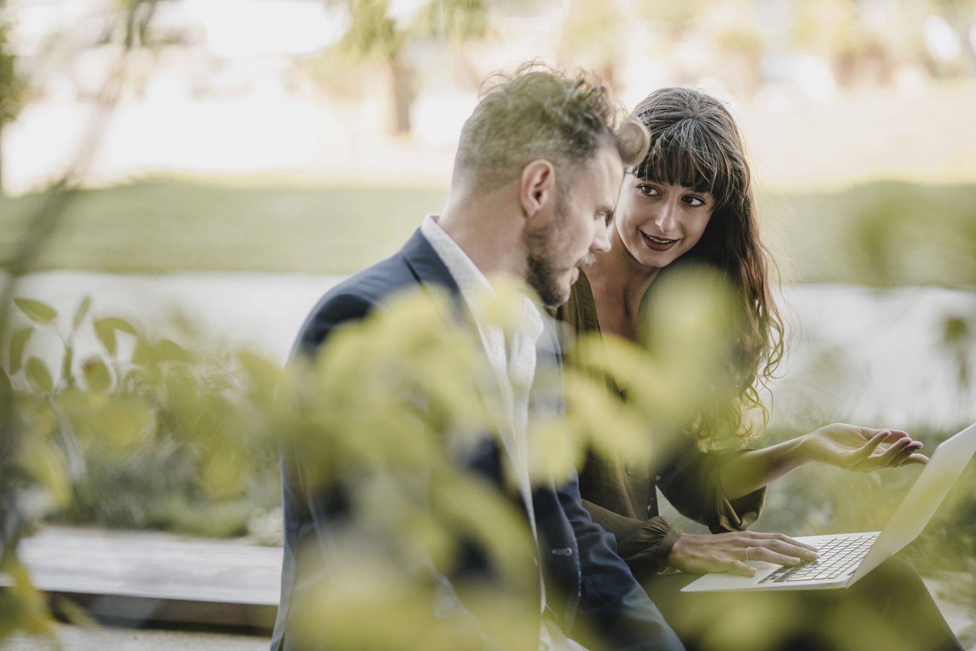 Un bărbat și o femeie se uită împreună la soluții tehnologice durabile pe un laptop în aer liber.