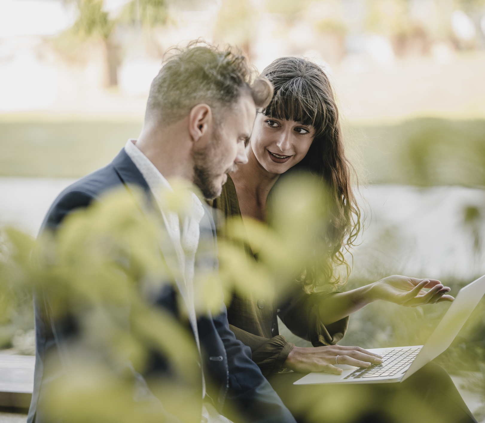 Un bărbat și o femeie stau afară și se uită la un laptop pentru a discuta despre soluții de gestionare a energiei.