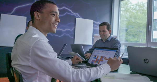 Angajați care lucrează la un laptop, sprijiniți de modelele de lucru flexibile și de echipamentele tehnologice ale CANCOM Austria.